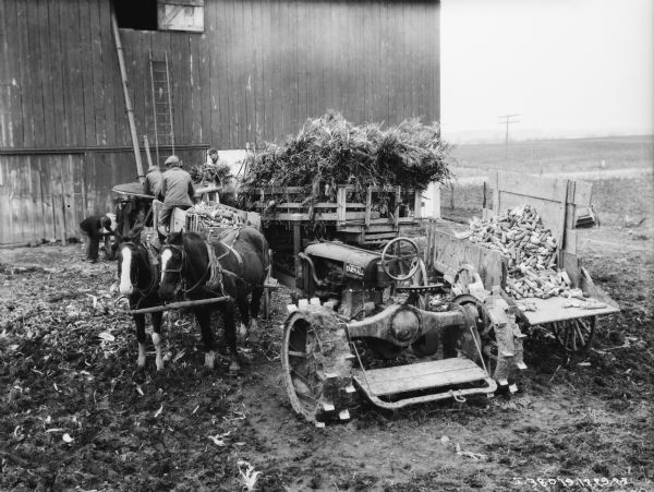 Slightly elevated view of men working with ensilage cutter near a barn.