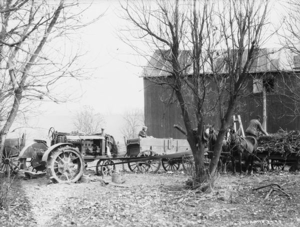 A group of men are using an ensilage cutter near a barn. A Farmall tractor on the left is belt driving the ensilage cutter. A young boy is sitting in the wagon in the center.