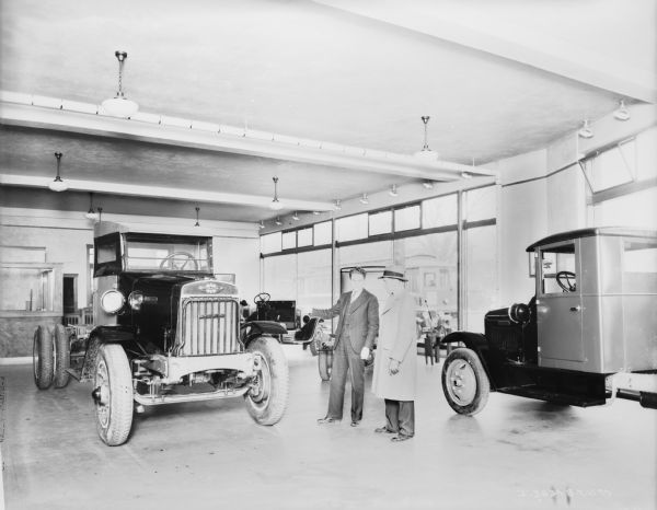 Salesman and client looking at trucks in a large showroom. Large show windows are along the wall in the background.