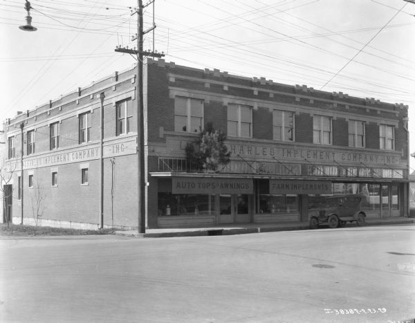 View across street towards a dealership. The sign on the front reads: "Lake Charles Implement Company Inc." There is a pine tree on display on the roof over the display windows of the dealership.