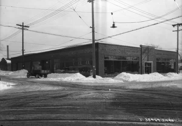 View from intersection towards a dealership on a corner. Snow is piled up along the curbs, and a truck is parked on the left along the curb.