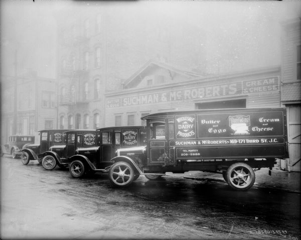 Suchman & McRoberts delivery trucks parked at an angle in a row in front of the Suchman & McRoberts building. The sign on the front read: "Butter & Eggs" and "Cream & Cheese."