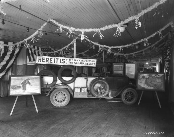View of a display of the truck that crossed the Sahara. Banners and flags are hanging around the room. A sign above the trucks reads: "Here It Is! The Truck That Crossed The Sahara Desert."