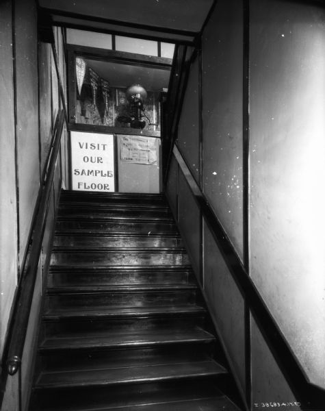 View up a stairway towards a sign that reads: "Visit Our Sample Floor."