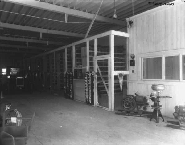 View of a parts storage area. There is a 3 H.P. McCormick-Deering Kerosene engine and a cream separator along the wall on the right. A truck is parked further down the parts storage area on the left.