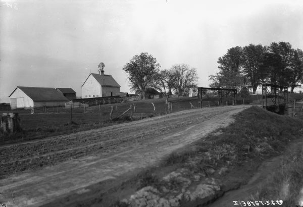 View of country road, bridge and farm buildings.