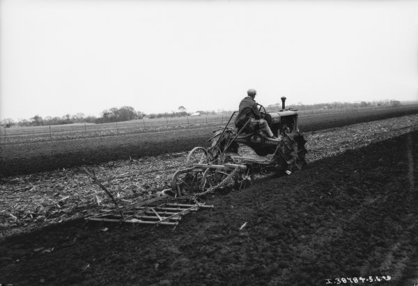 Rear view of a man driving a tractor pulling agricultural implements in a field.