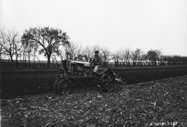 View towards a man using a Farmall tractor to pull an agricultural implement in a field.