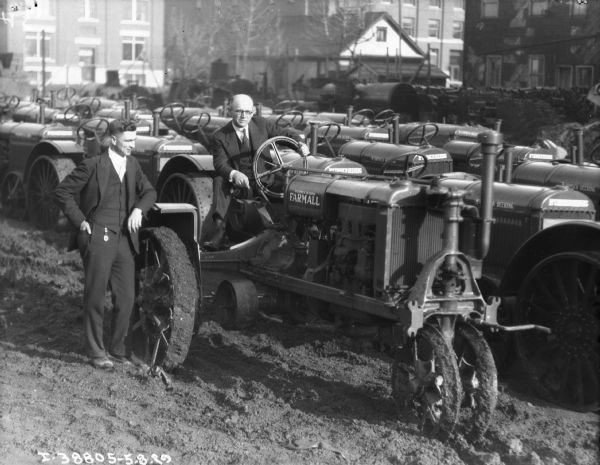 Two men are posing in a large yard full of Farmall tractors.