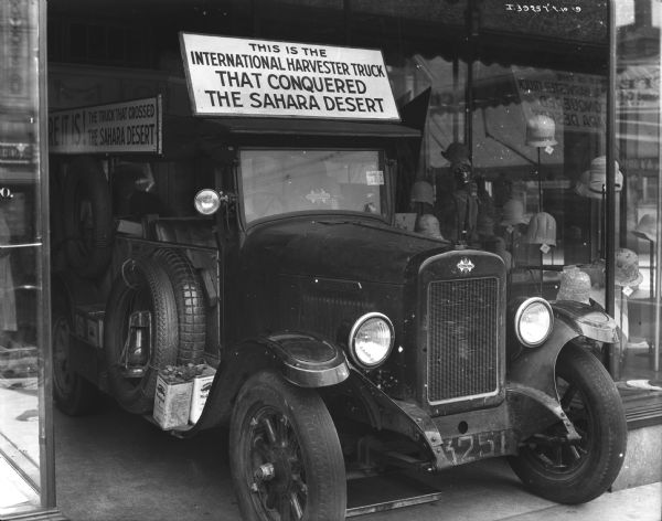 The truck is being displayed in the entrance to a hat store. A sign on the truck reads: "This is the International Harvester truck that conquered the Sahara Desert."
