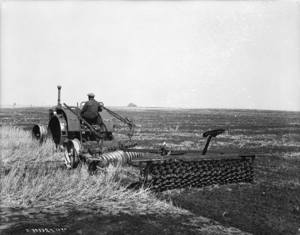 Man driving tractor-drawn cultipacker in a field.