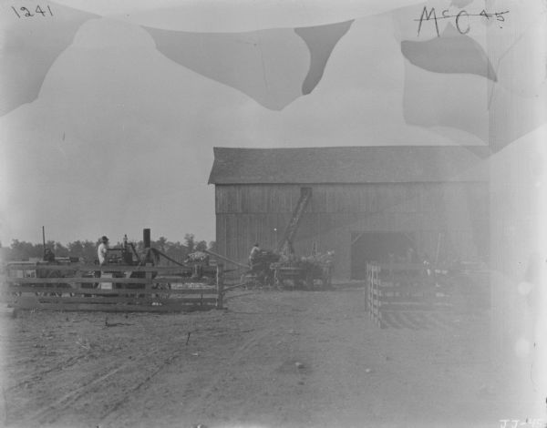 View towards three men using a husker and shredder in a barnyard.