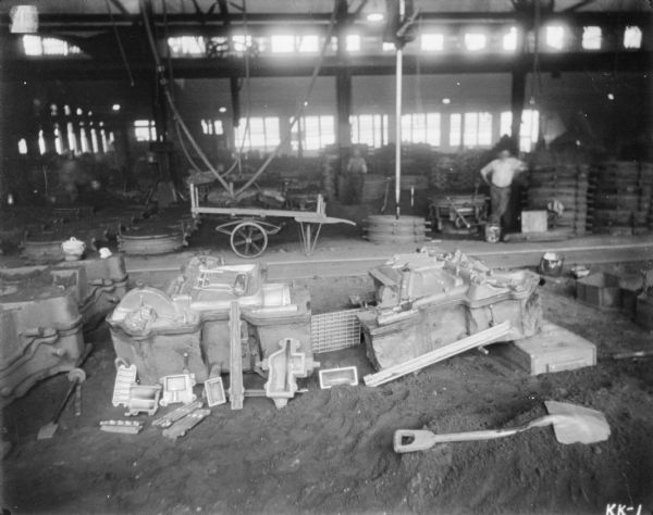 View of molds used to create machine parts in a factory. Men are standing in the background.