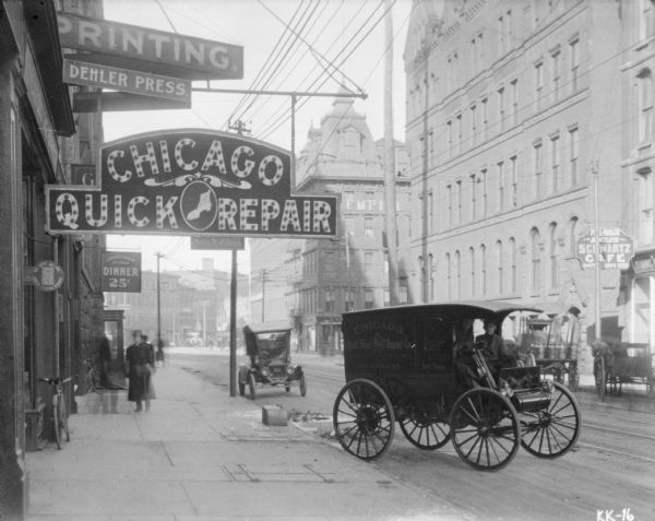 View down sidewalk towards a delivery truck for "Chicago Quick Shoe Repair" in front of the storefront for the repair business at 120 James Street. Across the street are horse-drawn wagons in front of the "Pool-Parlor Adolph Schwartz Café."