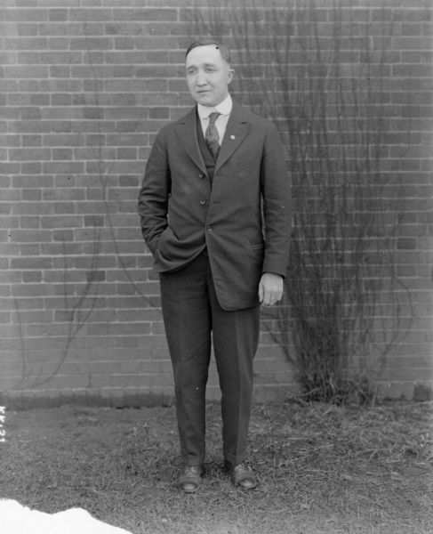 A man is standing on the grass outdoors in front of a brick wall.