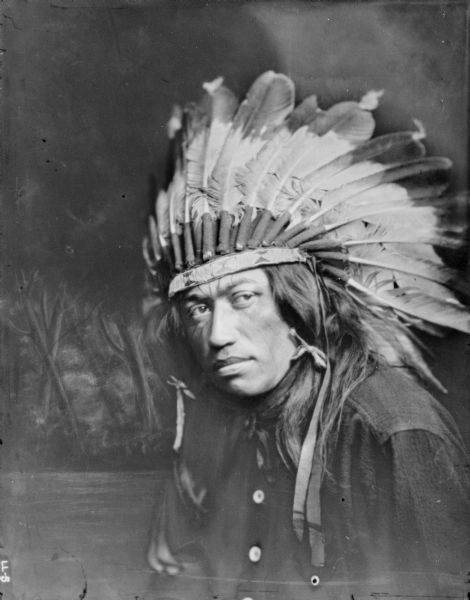 Quarter-length portrait in front of a painted background of a man wearing a Native American headdress.