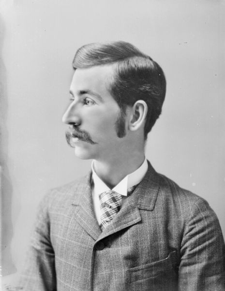 Waist-up portrait of young man with a moustache.
