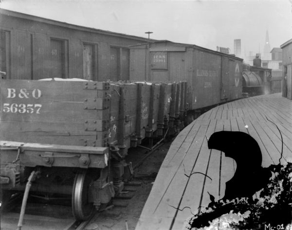 View from platform towards a line of boxcars on railroad tracks.