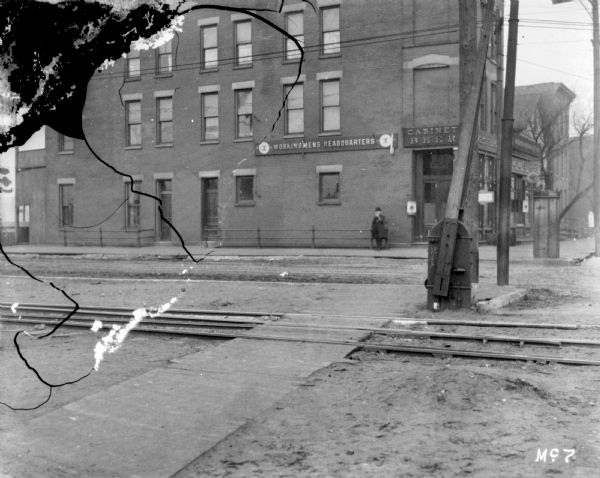 View across street towards the exterior of the bar at Workingmen's Headquarters. A man is standing on the sidewalk in front of the building.