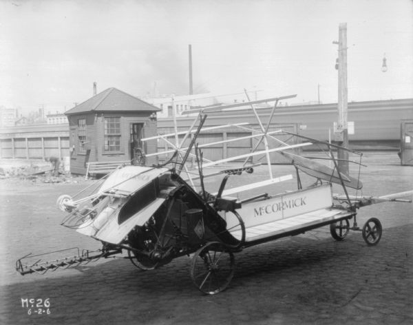 A McCormick Binder is parked outdoors. There is a man working near a small building in the background.