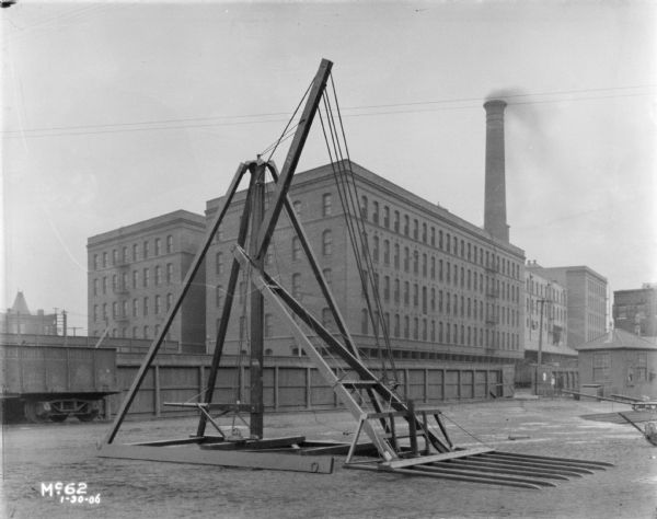 View towards a hay stacker set up in the yard of McCormick Works. A fence and buildings are in the background.