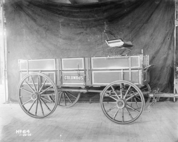 View towards the right side of a wagon parked on a wooden floor. There is a dark backdrop in the background.