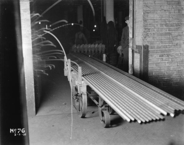 Cartload of long pipe at McCormick Work. A man is standing just inside the open door on the right.