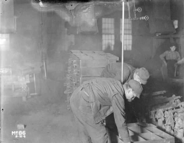 Two men are bending over while working in the foundry area in McCormick Works. Other workers are in the background.