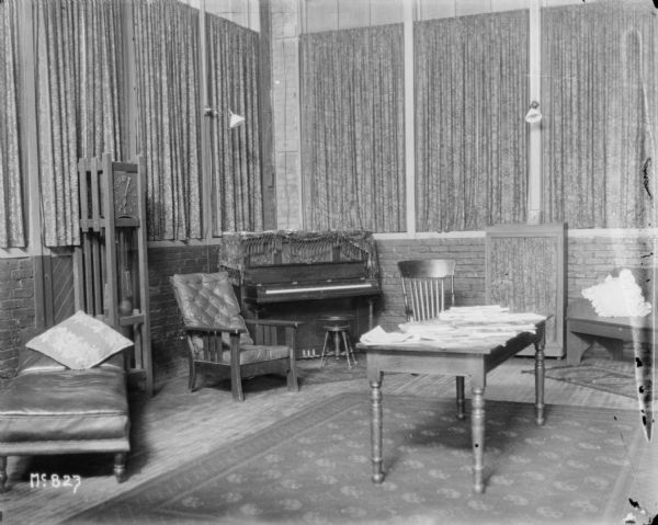 Waiting room. There is a lounge chair, a large clock against the wall on the right, and a piano in the corner. A stack of other papers are on a table on the right.