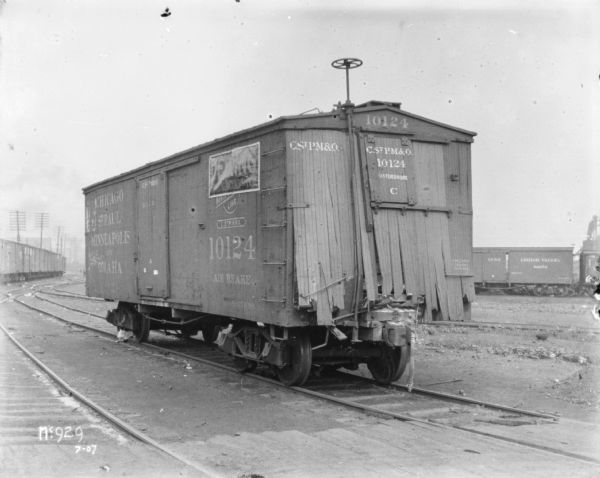 Boxcar at McCormick Works. There is a poster on the side that reads: "Deering Threshing Machines." The front wall of the boxcar is burst out. Perhaps from an accident or contest.