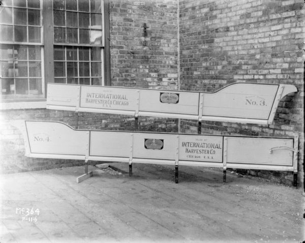 Boxes for two models of manure spreaders set up outdoors at the corner of a brick factory.