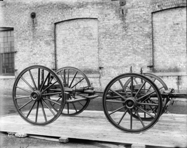 Weber wagon, without wagon box, outdoors at McCormick Works. A brick factory building is in the background.