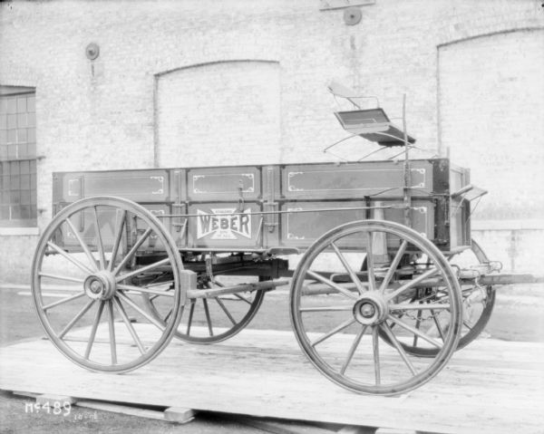 Weber wagon with wagon box set up outdoors on a wooden pallet at McCormick Works. There is a brick factory building in the background.