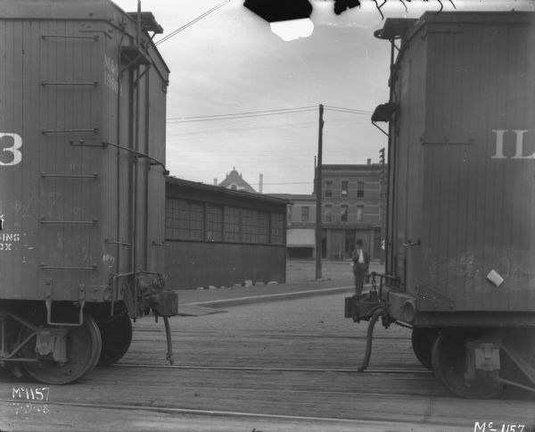 View between two railroad cars on railroad tracks at McCormick Works. A man is standing in the background.