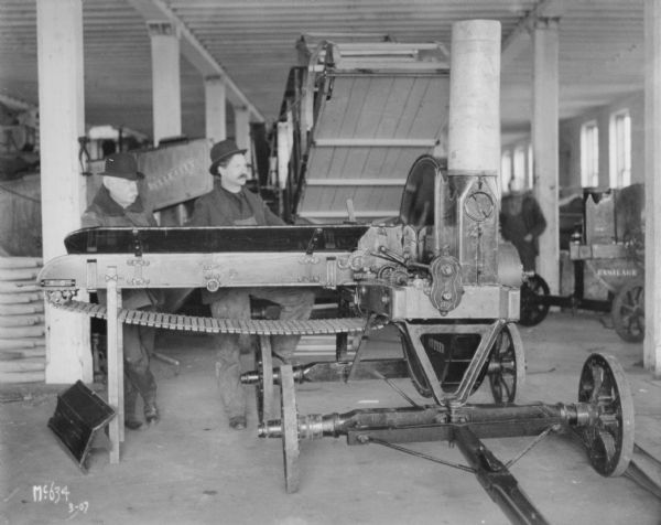 Two men are standing indoors with an ensilage cutter.
