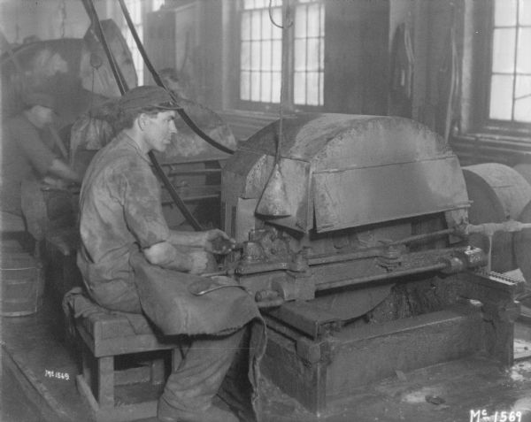 Man working at manufacturing machine at McCormick Works. Another man is working behind him on the left.