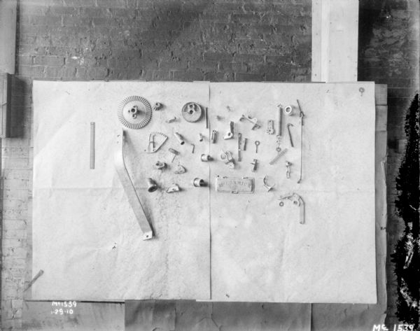 Parts mounted on paper on brick wall.