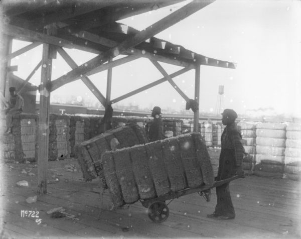 Men unloading manila or cotton at McCormick Works, under a partially covered loading dock. There is a water tower in the distance.
