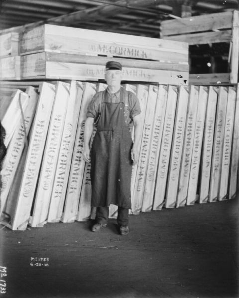 A man wearing an apron is standing in front of a stack of wood crates that have a stamp that reads "McCormick."