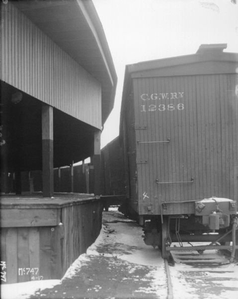 Railroad boxcars around a covered platform of a building. Snow is on the ground.