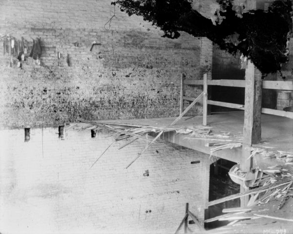 View towards collapsed floor on second level, with factory floor below. Brick wall along opposite side.