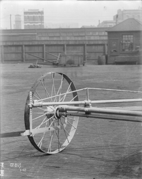 Close-up of a wheel on a Push Binder Header outdoors in a yard at McCormick Works. There is a small building and a fence in the background.