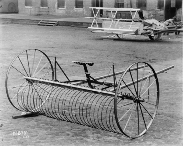 Rear view of a Dump Rake outdoors at McCormick Works. A man is working with an agricultural machine in the baqckground.