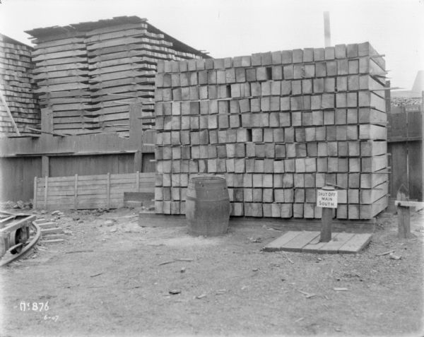 Lumber in stacks outdoors at McCormick Works. A sign on a pipe reads: "Shut Off Main South.