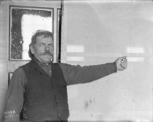 View of a man standing with his arm outstretched in an examining room at McCormick Works. This was possibly to measure arm length. The man has his thumb up, and his fist clenched.