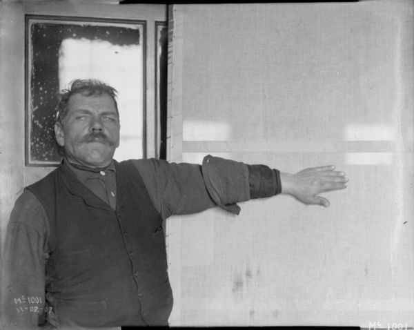 View of a man standing with his arm outstretched in an examining room at McCormick Works. This was possibly to measure arm length. The man has his thumb thumb down, and hand flat.