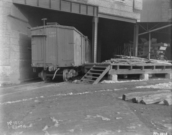 View towards a railroad car on railroad tracks partway under a building near a loading dock.
