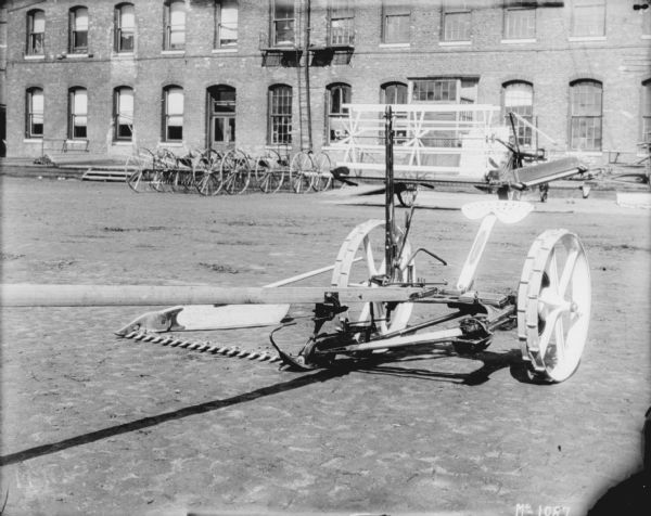 Horse-Drawn Mower outdoors in the yard at McCormick Works. There is a brick factory building in the background.