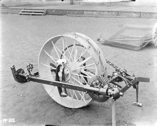 Wheels and chain drive of binders outdoors at McCormick Works. A loading dock and brick factory building are in the background.
