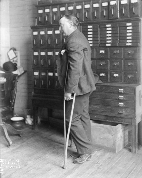 Man wearing a suit on crutches standing inside an office at McCormick Works.